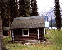 Side elevation of the Jacques Lake Warden Cabin Tack Shed, showing the the brown stain finish of the logs and the whitewashed log ends, 1996.; Parks Canada Agency/ Agence Parcs Canada, 1996.