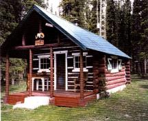 General view of Rocky Forks Warden Cabin showing its log-framed sheltered porch area at the entrance gable.; Agence Parcs Canada / Parks Canada Agency, 1996.