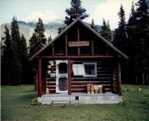Front elevation of the Adolphus Warden Patrol Cabin, showing its log-framed open porch with trussed-purlin supports and posts at the gable end, 1997.; Parks Canada Agency / Agence Parcs Canada, 1997.