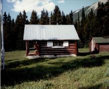 Side view of the Adolphus Warden Patrol Cabin, showing its walls of peeled logs, horizontally laid and saddle-notched at the corners, 1997.; Parks Canada Agency / Agence Parcs Canada, 1997.