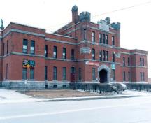 Front elevation of the Armoury, showing the simulated features typical of medieval military construction that include crenellated turrets, chimneys, and a massive troop doorway, 1989.; Department of National Defence / Ministère de la Défense nationale, 1989