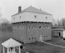 Vue en angle du Blockhaus, qui montre la volumétrie carrée de trois étages avec un toit pyramidal percé de cheminées, 1991.; Parks Canada Agency / Agence Parcs Canada, 1991.
