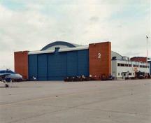 General view of Hangar 2 demonstrating the high, wide doorways that span its east and west elevations, the raised central sections for particularly high aircraft, and the brick pylons at each end, 2000.; Department of National Defence / Ministère de la Défense nationale, 2000.