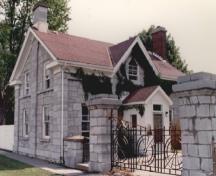 Vue générale du bâtiment 6 du CMR, qui montre son aspect d’habitation revêtue de pierre, avec un toit à deux versants présentant un pignon central à l’avant et à l’arrière et des cheminées aux extrémités, 1993.; Parks Canada Agency / Agence Parcs Canada, 1993.