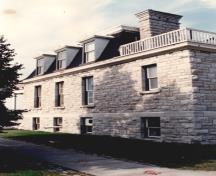View of the side of RMC Building 55, showing the continuous stone string course and wall surfaces, and the eave mouldings, 1993.; Parks Canada Agency / Agence Parcs Canada, 1993.