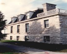 Vue du côté du bâtiment 55 du CMR, qui montre le cordon continu, les surfaces des murs et les moulures de l’avant-toit, 1993.; Parks Canada Agency / Agence Parcs Canada, 1993.