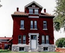 Vue générale du bâtiment 5 du CMR, qui montre les détails en pierre, dont l’assise du bâtiment, les linteaux et appuis, les cartouches portant des inscriptions en relief et l’ornementation autour de l’entrée, 1993.; Parks Canada Agency / Agence Parcs Canada, 1993.