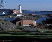 Vue panoramique du Projecteur n° 7 démontrant l’effort délibéré qui a été déployé pour créer l’impression que la structure est une remise à bateau, avec un bateau et des planches disposés sur un affleurement rocheux au bord de l’eau, 2003.; Parks Canada Agency / Agence Parcs Canada, C. Cheadle, 2003.
