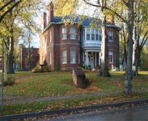 Vue générale de la villa Fairholm démontrant les fenêtres en saillie légèrement arrondies sur toute la hauteur de la façade, les larges avant-toits, et le vaste terrain entourant la villa, 2006.; Parks Canada Agency / Agence Parcs Canada, 2006.