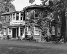 Corner view of the Fairholm villa showing the mottled red brick walls; and cut stone used as lintels over the windows, for the raised basement, and as a string course between the two storeys.; Parks Canada Agency / Agence Parcs Canada, n.d.