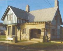 Exterior view of the Belmont Road Main Gatehouse, showing its Tudor Revival details such as half-timber construction, irregular rubble masonry walls,  buttresses, and gently tapered chimneys, dressed quoins and corbels, and the entrance porch with its sto; Department of National Defence/Ministère de la Défense nationale, D. Cebula, 2000.