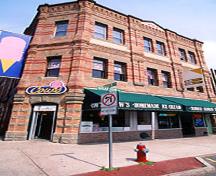 Vue générale de Apothecaries Hall démontrant sa masse rectangulaire à trois étages surmontée d'un toit plat et ses grandes vitrines au rez-de-chaussée, 1995.; Parks Canada Agency / Agence Parcs Canada, J. 	Butterill, 1995.