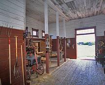 Interior view of the Sick Horse Stable, showing the interior configuration of central combined driveway and feed alley that serves the single standing stalls and the box stall, 2003.; Parks Canada Agency / Agence Parcs Canada, M. Fieguth, 2003.