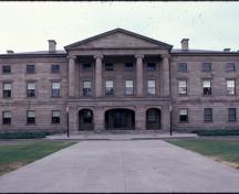Vue générale montrant le volume symétrique de l’édifice de trois étages, qui est formé d’un corps central, d’ailes offrant un bel équilibre visuel et d’un toit en croupe peu élevé.; Parks Canada Agency / Agence Parcs Canada