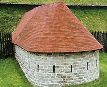 Vue en angle de la caponnière, qui montre sa volumétrie géométrique simple et son toit incliné, revêtu de bardeaux métalliques, qui est courbé à l’extrémité sud, 1972.; De Jonge, Parks Canada Agency / Agence Parks Canada, W. Wyett, 1972