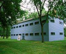 Rear view of the Men's Two-Storey Barracks, showing regular, horizontally aligned windows and a low, hipped roof, 1994.; Parks Canada Agency / Agence Parcs Canada, B. Morin, 1994.