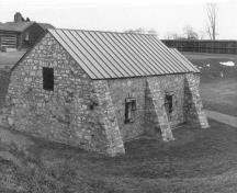 Vue en arrière de la poudrière, qui montre sa volumétrie extérieure, avec des contreforts qui renforcent l’ensemble, 1989.; Parks Canada Agency / Agence Parcs Canada, 1989.