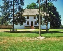 General view of the front facade of the Big House showing its two-storey rectangular structure that is five bays in length and three bays in width,
with a hipped roof and front verandah, 2002.; Parks Canada Agency / Agence Parcs Canada, M. Trepanier, 2002.