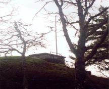 Vue générale du poste du commandant de la batterie montrant le volume simple sur un étage, coiffé d’un toit plat, de ce bâtiment qui est partiellement dissimulé par un remblai de terre, 1997.; Parks Canada Agency / Agence Parcs Canada, J. Mattie, 1997.