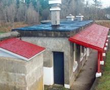 Vue de côté du Poste de garde mettant de l'emphase sur le porche en pente douce, avec ses poutres apparentes, le revêtement du toit et les cinq poteaux de bois chanfreinés, 1997.; Parks Canada Agency / Agence Parcs Canada, J. Mattie, 1997.