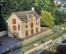 Vue générale du bâtiment de l’intendance, qui montre le toit à deux versants et la concentration des grandes portes de livraison, 2002.; Parks Canada Agency / Agence Parcs Canada, A. Guindon, 2002.