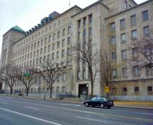 Vue générale de l'Édifice commémoratif de l'ouest montrant les volumes en gradins, les détails aplatis, les piliers élevés et peu profonds entre les fenêtres, 2011.; Parks Canada Agency / Agence Parcs Canada, M. Therrien, 2011.