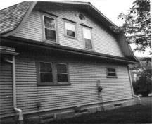 Side view of the Superintendent's Residence showing its exterior covered with clapboard on the ground storey and wooden shingles on the gable ends and sides of the dormers, 1984.; Parks Canada Agency / Agence Parcs Canada, R. Stuart, 1984.