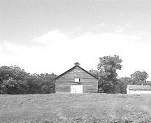 Vue de l'extérieur de l’écurie de fort Dufferin, qui montre son emplacement relativement isolée dans un pré.; Parks Canada Agency / Agence Parcs Canada.