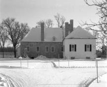 Rear view of the Big House, showing its two linked structures, both of which have prominent hipped roofs and masonry chimneys, 1989.; Parks Canada Agency / Agence Parcs Canada, 1989.