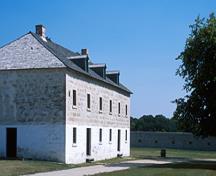 Corner view of the Warehouse showing the medium-pitched hipped roof with gabled dormers and two stone chimneys and the arrangement of windows and doors, 2003.; Parks Canada Agency / Agence Parcs Canada, G. Kopelow, 2003.