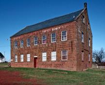 Vue générale de la Banque des fermiers de Rustico qui montre la masse solide, à deux étages et demi, surmontée d’un toit moyennement incliné.; Parks Canada Agency / Agence Parcs Canada.