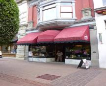 Vue générale de l'Édifice Rogers, qui montre la devanture de la boutique, et notamment le vitrage orné avec un auvent délicat aux fenêtres à carreaux sertis de plomb qui surplombe l'entrée en retrait, 2011.; Parks Canada Agency / Agence Parcs Canada, Andrew Waldron, 2011.