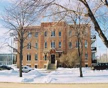 This image illustrates the overall form and massing of the Ross Flats Apartment, in its prominent river valley location. The facades are constructed of brick and the end balconies are from wood. ; City of Edmonton, 2004