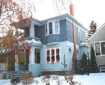 This image illustrates the two-storey south and west wood-clad facades of the Roy Gerolamy Residence with hipped-roof and asymmetrically-located two-storey veranda, front upper floor bay window, side chimney, and west facade bay window with hipped roof.; City of Edmonton, 2004