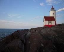 Vue du phare de l'Île Verte et du bâtiment de la corne de brume sur le terrain en rochers plats; Agence Parcs Canada | Parks Canada Agency, Valérie Busque, 2009.