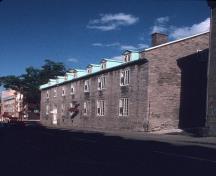 Vue en angle du 57-63, rue Saint-Louis montrant l’uniformité des détails: fenêtres à battants à lumières multiples, portes à imposte donnant directement sur la rue et chaînes d’angle et seuils en pierre contrastante.; Parks Canada Agency / Agence Parcs Canada
