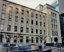 Vue générale de l'Édifice commémoratif de l'Est montrant les volumes en gradins, les détails aplatis, les piliers élevés et peu profonds entre les fenêtres de la façade principale, 2011.; Agence Parcs Canada / Parks Canada Agency, 1995.