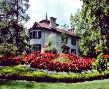 Vue générale de la villa Bellevue, qui montre les murs en calcaire de la région et l’emploi de crépi blanc sur les murs, style inspiré des villas italianisantes basées sur la conception pittoresque britannique, 1977.; Parks Canada Agency / Agence Parcs Canada, Mackenzie, 1977.