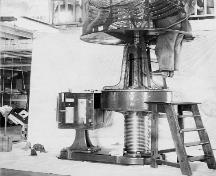 Historic photograph taken in New Férolle Peninsula Lighthouse showing a man working in the lense.; Library and Archives, Department of Transports, Marine Aids Division | Bibliothèque et Archives Canada, ministère des Transports, division des aides maritimes, e0003719347.