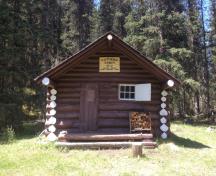 View of the front entrance of the Cuthead Warden Cabin, showing a low-pitched roof, gabled ends and a sheltered off-centered entrance porch with verandah, 1996.; Parks Canada Agency / Agence Parcs Canada, 2018, Mitch Fennel.