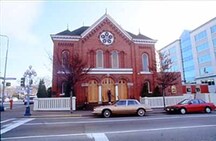 Vue de l'extérieur de la synagogue de la congrégation Emanu-el, qui montre la fenêtre circulaire sur le pignon à fronton, 1994.; Parks Canada Agency / Agence Parcs Canada, J. Butterill, 1994.