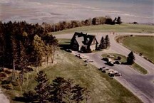 Bird's eye view of the Visitor Information Centre East, showing the building’s picturesque design and location in an open setting which in turn emphasizes the rustic nature of the setting, c. 1980.; Parks Canada Agency / Agence Parcs Canada, c./vers 1980.