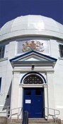 Vue générale du lieu historique national du Canada l'Observatoire-Fédéral-d'Astrophysique montrant son portique d'entrée en saillie avec des colonnes latérales qui soutiennent un petit toit à fronton et d'un entablement aux armoiries du Dominion du Canada; Parks Canada Agency/Agence Parcs Canada, Andrew Waldron, 2008