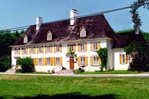 Vue générale du manoir Mauvide-Genest, qui montre l’imposante volumétrie rectangulaire de deux étages du corps principal de la résidence, avec son toit à quatre versants abrupts, que ponctuent de petites lucarnes et deux grandes cheminées.; Parks Canada Agency / Agence Parcs Canada.