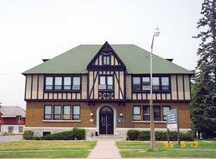 Vue de l'extérieur du bâtiment de l'horticulture, qui montre l’entrée principale placée au centre, sous un arc en pierre, et une travée centrale en saillie avec un toit à pignon qui perce la ligne faîtière, 1995.; Department of Agriculture / Ministère de l'Agriculture, Patricia Armstrong, 1995.