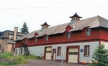 Vue en angle de l'élévation nord du Bâtiment de service montrant le toit en croupe revêtu de bardeaux avec un large surplomb et des consoles sculptées, les ventilateurs de toit décoratifs, les lucarnes et l’avant-toit arrondi au-dessus des fenêtres, 1995.; Parks Canada Agency / Agence Parcs Canada, C. Zacconi, 1995.