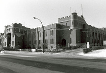 Vue en angle du manège militaire Mewata, qui montre un des quatre tours d’angle crénelées à trois étages, carrées et massives, semblables à des bastions, reliées entre elles par des murs extérieurs à créneaux, 1983.; Department of National Defence / Ministère de la Défense nationale, 1983.
