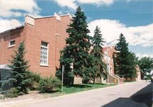 Vue de la façade principale du bâtiment du gymnase et de la piscine de la GRC, qui montre les murs-pignons à redans surélevés surmontés d’un couronnement de pierre blanche décoratif, 1986.; Royal Canadian Mounted Police / Gendarmerie royale du Canada, 1986.